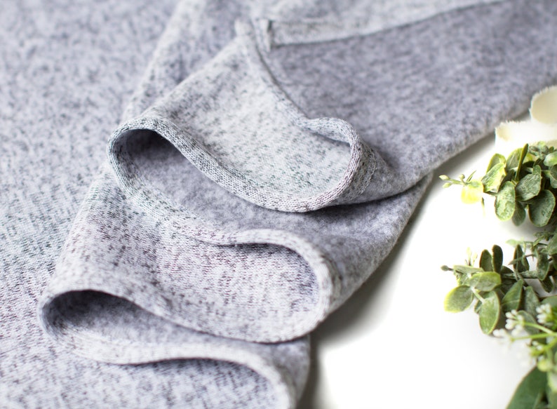 May include: Close-up of a gray, textured fabric with a soft, crinkled appearance. The fabric is folded over itself, creating a series of folds and creases.