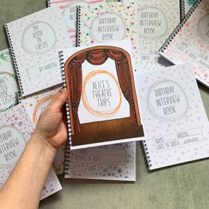 Puede incluir: Una colecci&oacute;n de libros encuadernados en espiral con varias portadas. Un libro presenta una ilustraci&oacute;n de un escenario teatral con el texto "ALICE'S THEATRE TRIPS". Otros libros incluyen "BIRTHDAY INTERVIEW BOOK" y "MY BOOK OF FIRSTS". Las portadas tienen patrones de estrellas y confeti.