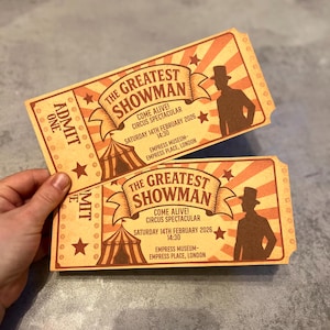 May include: Two rectangular paper tickets with a vintage orange and cream sunburst background. The text reads THE GREATEST SHOWMAN, COME ALIVE! CIRCUS SPECTACULAR, SATURDAY 14TH FEBRUARY 2026, 14:30, EMPRESS MUSEUM, EMPRESS PLACE, LONDON. Features a circus tent and a top-hatted figure.