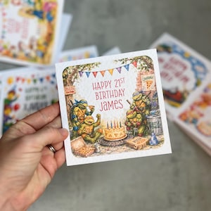 May include: A square birthday greeting card featuring a colourful illustration of four Teenage Mutant Ninja Turtles characters celebrating with pizza and a cake. The text reads Happy 21st Birthday James. The card has a textured white paper finish.