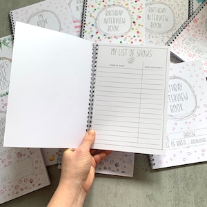 Puede incluir: Un libro de entrevistas de cumplea&ntilde;os con encuadernaci&oacute;n en espiral y dise&ntilde;o de confeti colorido. La p&aacute;gina abierta muestra una lista titulada "MY LIST OF SHOWS" con espacios para el nombre del programa y la fecha. Se ven otros libros con dise&ntilde;os similares.