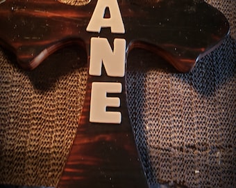 May include: A wooden cross with a dark brown stain and a white painted name "LANE" on the front.