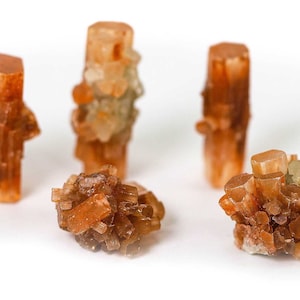 May include: Five brown and orange crystal clusters, some with a cross-like shape, on a white background.