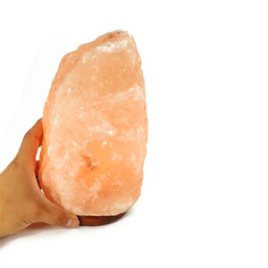 May include: A large, natural Himalayan salt lamp with a warm orange glow. The lamp is made of a single, irregularly shaped piece of salt and sits on a wooden base.
