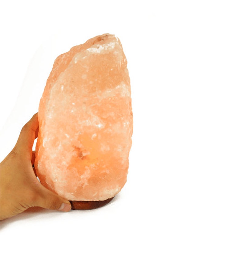 May include: A large, natural Himalayan salt lamp with a warm orange glow. The lamp is made of a single, irregularly shaped piece of salt and sits on a wooden base.