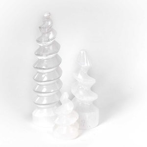Puede incluir: Tres esculturas de cristal de selenita blanco en forma de espiral. Las esculturas son de diferentes tamaños y están dispuestas en fila.