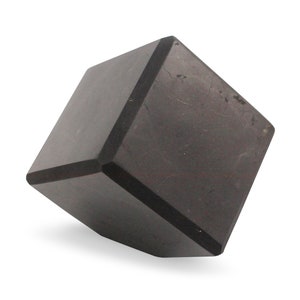 May include: A dark gray, cube-shaped object with beveled edges. The cube is positioned at an angle, showcasing its geometric form. The surface has a slightly textured appearance, and the overall aesthetic is minimalist.