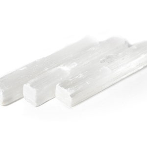 May include: Three white selenite wands, also known as selenite sticks, are arranged side by side on a white background. The wands are smooth and have a natural, striated texture.