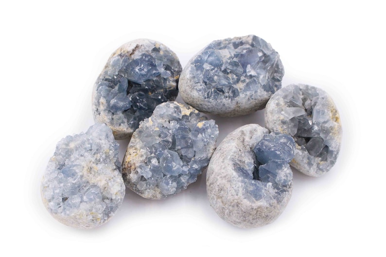 May include: Six blue celestite crystal clusters, each with a unique shape and size, are arranged on a white background. The crystals have a natural, rough texture and a light blue color.