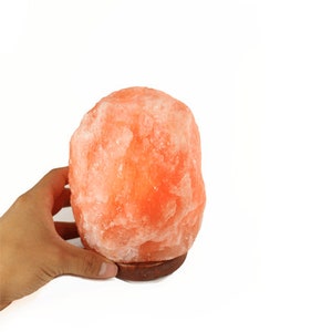 May include: A pink Himalayan salt lamp with a wooden base. The lamp is lit and glowing orange.