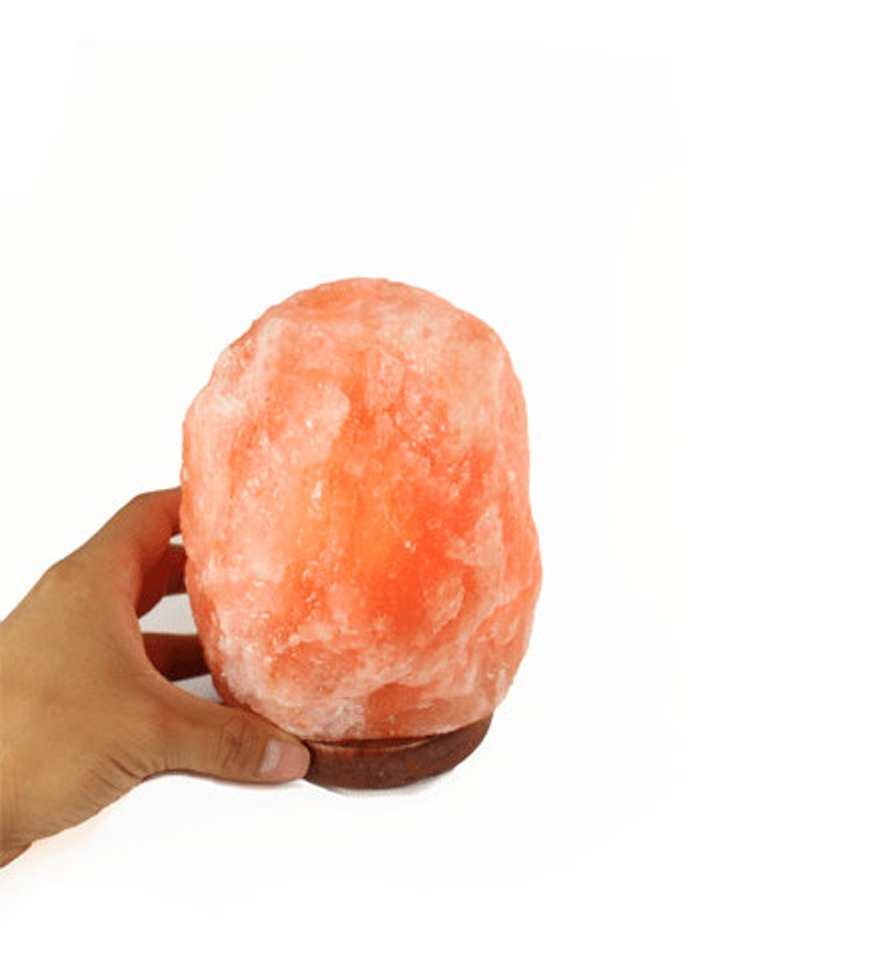 May include: A pink Himalayan salt lamp with a wooden base. The lamp is lit and glowing orange.