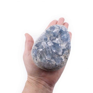 May include: A large, light blue crystal cluster with a rough, natural texture. The crystal is held in a hand, showcasing its size and shape.