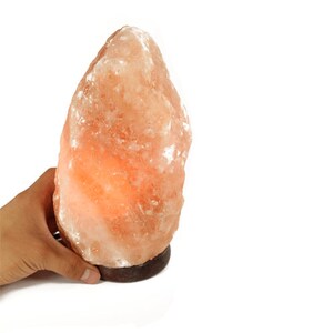 May include: A large, natural Himalayan salt lamp with a warm orange glow. The lamp is made of a single piece of salt and has a wooden base.
