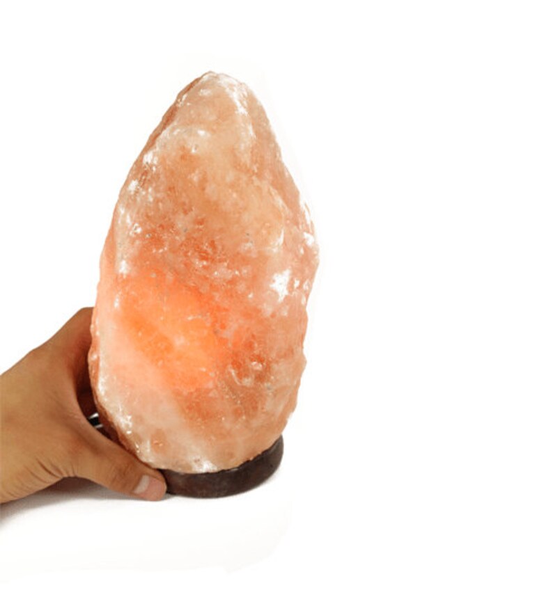 May include: A large, natural Himalayan salt lamp with a warm orange glow. The lamp is made of a single piece of salt and has a wooden base.