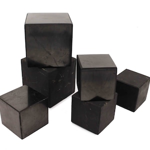May include: A set of six black obsidian cubes of varying sizes. The cubes are smooth and polished, with a slight sheen. They are arranged in a pyramid shape, with the largest cube at the top.