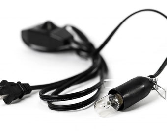 Könnte beinhalten: Ein schwarzes Stromkabel mit einem Stecker an einem Ende und einer Lampenfassung am anderen. Das Kabel ist aufgerollt und die Lampenfassung ist leer.