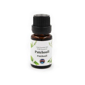 Puede incluir: Una pequeña botella de vidrio marrón con una tapa negra, que contiene aceite esencial de Pachulí. La etiqueta es blanca con hojas verdes y el texto "Huile Essentielle 100% PURE Essential Oil Patchouli Patchouli".