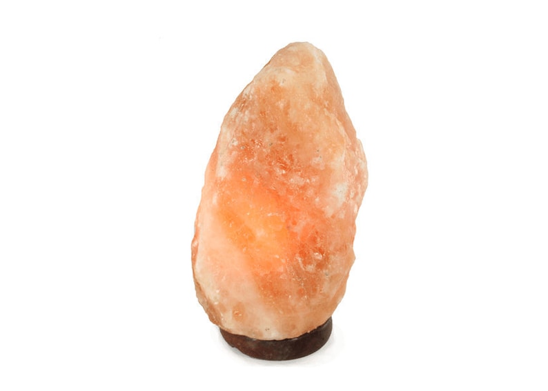 May include: A large, orange-colored Himalayan salt lamp with a wooden base. The lamp is lit and glowing.
