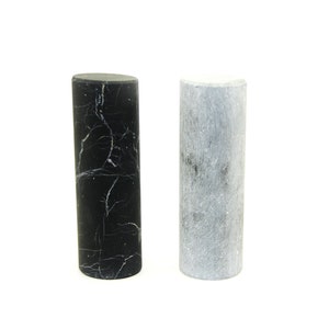 May include: Two cylindrical marble rolling pins, one black and one gray.
