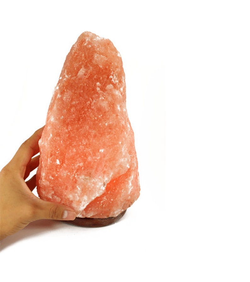 May include: A large, pink Himalayan salt lamp with a wooden base. The salt lamp is irregularly shaped and has a rough, textured surface.