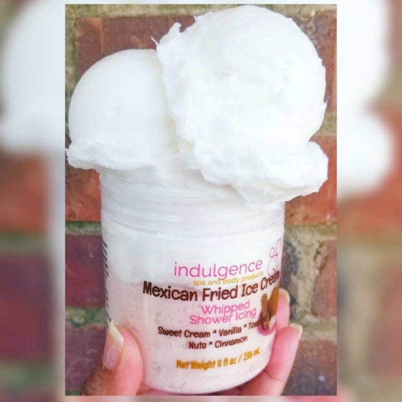 Pu&ograve; includere: Un barattolo bianco con un'etichetta rosa che recita "indulgence spa and body products Mexican Fried Ice Cream Whipped Shower Icing Sweet Cream Vanilla Toppings Nuts Cinnamon Net Weight 8 fl oz / 236 ml". Il barattolo &egrave; sormontato da due cumuli di panna montata bianca.