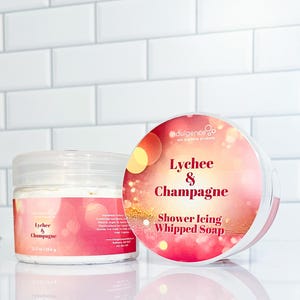Pu&ograve; includere: Un barattolo da 354 g di sapone montato per la doccia al litchi e champagne. Il barattolo &egrave; bianco con un'etichetta rosa e dorata. L'etichetta riporta il testo "indulgence spa and body products" e "Lychee & Champagne Shower Icing Whipped Soap".