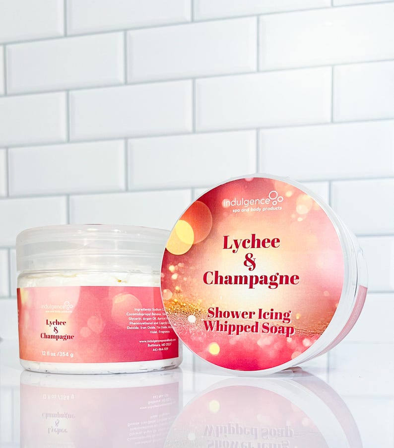 Pu&ograve; includere: Un barattolo da 354 g di sapone montato per la doccia al litchi e champagne. Il barattolo &egrave; bianco con un'etichetta rosa e dorata. L'etichetta riporta il testo "indulgence spa and body products" e "Lychee & Champagne Shower Icing Whipped Soap".