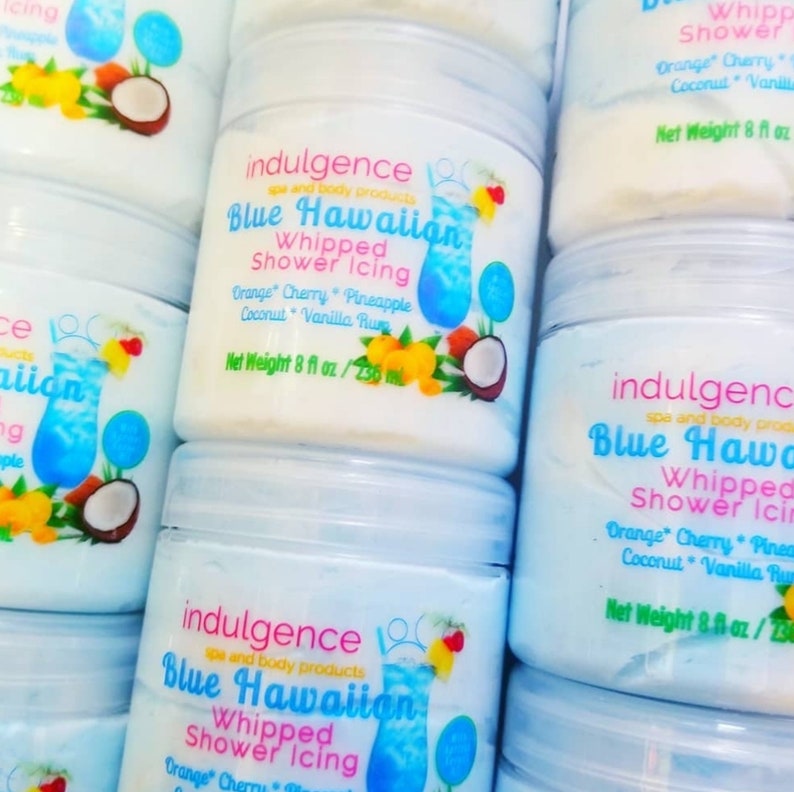 Pu&ograve; includere: Tre barattoli di glassa per doccia montata Blue Hawaiian. I barattoli sono etichettati con il nome del prodotto, gli ingredienti e il peso netto. I barattoli sono impilati uno sopra l'altro.