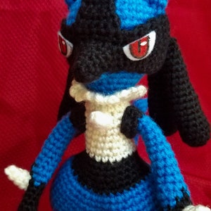 Puede incluir: Un juguete de peluche azul y negro tejido a crochet con ojos rojos. El juguete es un personaje popular de un videojuego y una serie de anime.