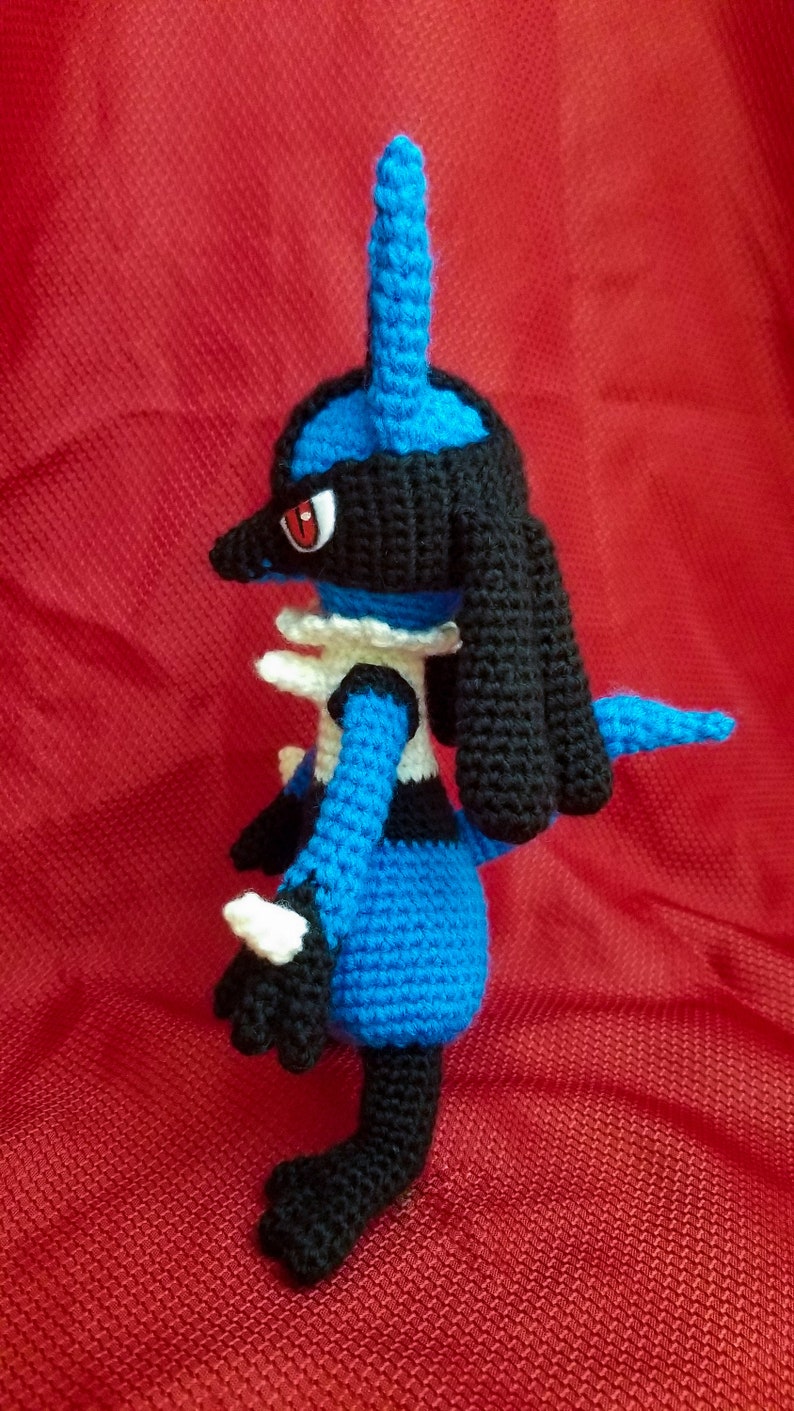 Puede incluir: Un juguete de peluche azul y negro de crochet de un personaje de Pokemon. El juguete tiene un cuerno azul largo y puntiagudo y una cola negra.