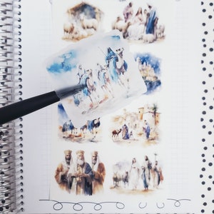 May include: A set of six watercolor Christmas stickers featuring scenes from the Nativity story. The stickers include images of the three wise men, the nativity scene, and other scenes from the Christmas story.