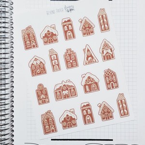 May include: Sheet of stickers featuring various gingerbread house designs in shades of brown and white. The stickers are arranged on a white background with a grid pattern and the text "BEYOND PAPER" and "Flowers" is visible.