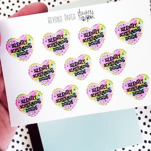 May include: A sheet of stickers featuring heart-shaped designs with the text "SILENTLY SCREAMING INSIDE." Each sticker has a rainbow gradient center, a scalloped border, and small flower and heart details. The brand name "BEYOND PAPER flowers" is printed at the top.