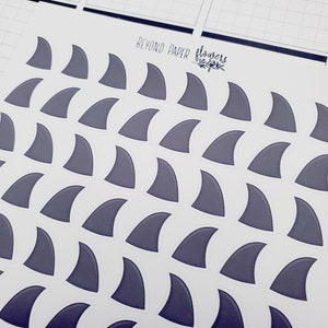 May include: A sheet of stickers featuring a repeating pattern of gray shark fin shapes. The sheet is white with the text "Beyond Paper" and "flowers" in black.