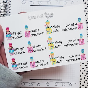 May include: Nine colorful stickers featuring a nutcracker character with different sayings. The sayings include "let's get crackin'," "what's crackin'?" "totally nuts," and "son of a nutcracker."