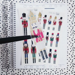 May include: A sheet of stickers featuring a variety of nutcracker designs. The stickers are printed on clear, glossy paper and feature a variety of colors, including red, blue, green, and gold. The stickers are perfect for adding a festive touch to any project.