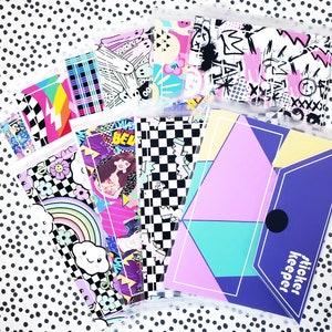 May include: A set of clear plastic sticker keeper pouches with colorful patterned designs. The pouches are labeled "sticker keeper" and feature various patterns including checkered, rainbow, and geometric designs.