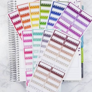 May include: A set of colorful planner stickers with a heart design and the days of the week abbreviated. The stickers are arranged in rows and columns on a white surface.