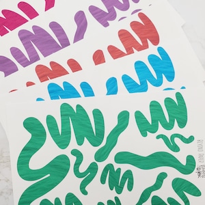 May include: A stack of white paper sheets with green, blue, light blue, orange, purple, and pink wavy lines printed on them. The paper sheets are stacked on a white surface. The text "Beyond Paper" is printed on the bottom right corner of the bottom sheet.