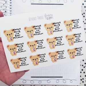 May include: A sheet of stickers featuring a cartoon bear holding a boba tea. The bear is wearing a light brown shirt and has a pink nose. The text on the stickers reads "always doing the bear minimum".
