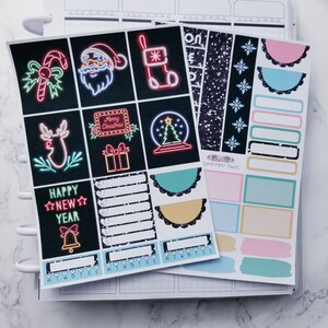 May include: A set of Christmas-themed planner stickers featuring neon lights, snowflakes, and a black and white glitter pattern. The stickers include images of a candy cane, Santa Claus, a stocking, a reindeer, a gift box, a snow globe, and a bell. The text "Happy New Year" is also included.