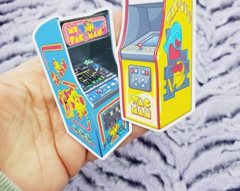 May include: Two vintage arcade game stickers. One is blue and yellow with the text "Ms. Pac-Man" and the other is yellow with the text "Pac-Man".