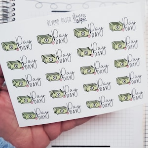 May include: A sheet of white planner stickers featuring green money stacks with a pink heart and the words "Pay Day" in black script. The stickers are from "Beyond Paper Flowers."