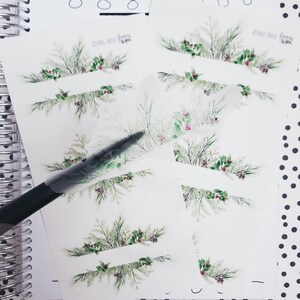 May include: A set of six printable Christmas-themed planner stickers featuring a watercolor design of green branches, red berries, and a white banner. The text "Beyond Paper Planners" is printed on the stickers.