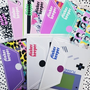May include: A collection of sticker keeper pouches in various colors, including pink, purple, and teal. Each pouch features the text "sticker keeper" in a contrasting color. The background is a white surface with black polka dots.