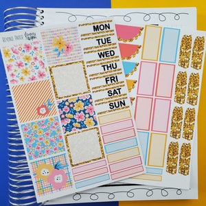 May include: A set of colorful planner stickers with floral patterns, gold glitter accents, and days of the week labels. The stickers are designed for use in a planner or journal.