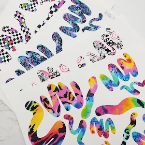 May include: A sheet of colorful patterned stickers with a variety of abstract shapes. The stickers feature a variety of patterns including animal print, tie-dye, and geometric designs. The stickers are printed on white paper and are ready to be cut out and used.