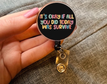 May include: A black retractable badge reel with the text "IT'S OKAY IF ALL YOU DID TODAY WAS SURVIVE" in colorful letters. The badge reel has a clear plastic cover and a metal clip.