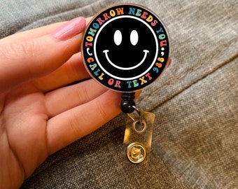 May include: A black and white smiley face badge with the text "Tomorrow Needs You... 988 - Call or Text" in rainbow colours around the edge.