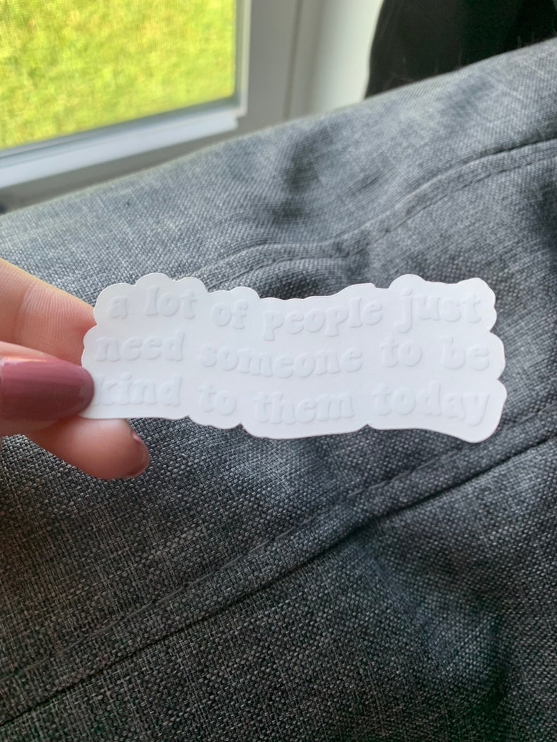 Op de afbeelding: Witte sticker met de tekst "veel mensen hebben gewoon iemand nodig die vandaag aardig tegen ze is".